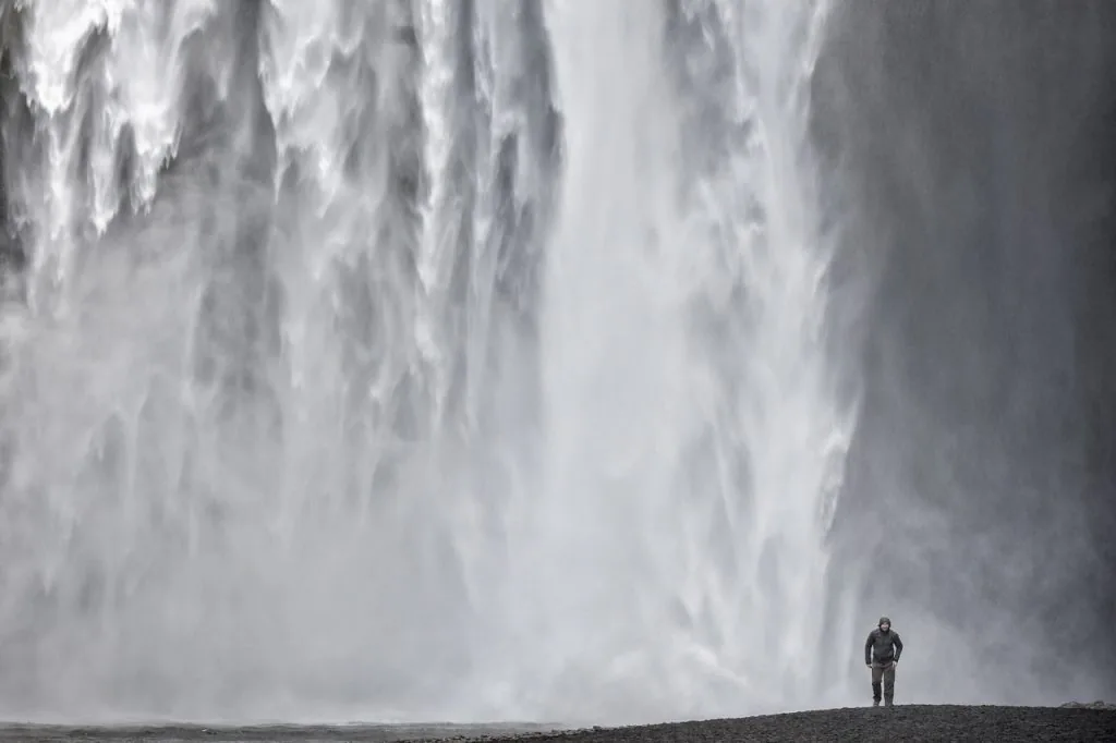 Cascata in Islanda tagliata dai bordi del fotogramma, con una piccola figura umana che ne suggerisce la grande dimensione