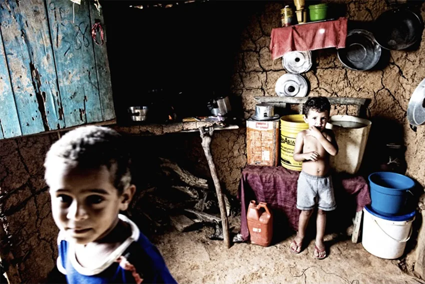 Bambino in primo piano in una favela brasiliana che fa da quinta, con la casa che si apre alle sue spalle