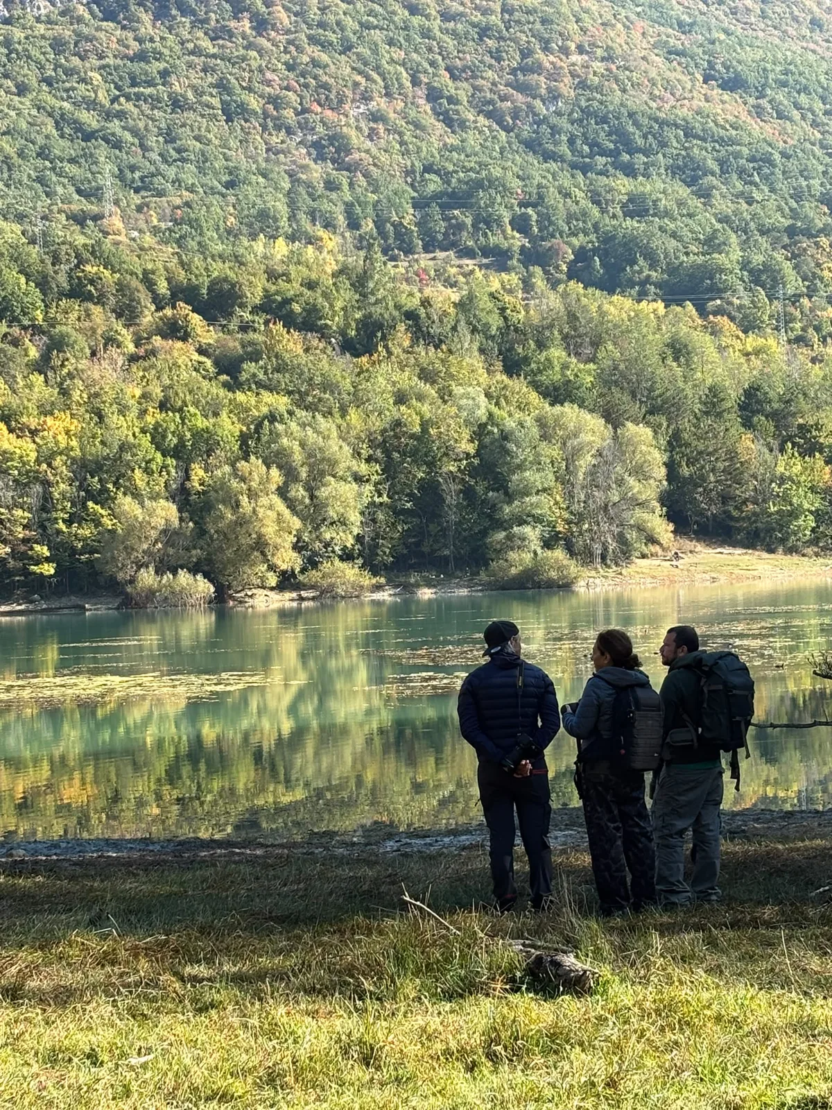 Partecipanti al workshop di fotografia sulla riva di un lago nel Parco Nazionale d'Abruzzo con il bosco autunnale riflesso